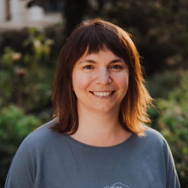 Kobieta w ciemnych włosach do ramion, ubrana w szarą bluzkę.