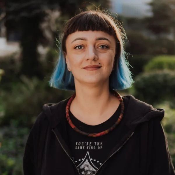 Kobieta w krótkich, niebiesko-brązowych włosach przed ramiona, ubrana na czarno.